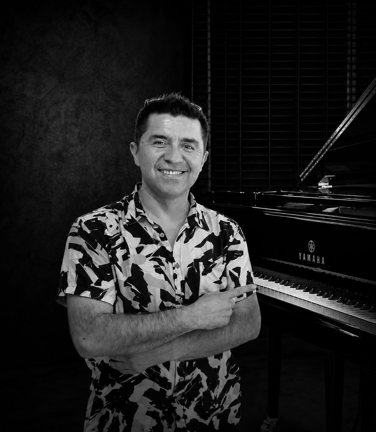 Retrato en blanco y negro de César Ibacache junto a un piano de cola Yamaha